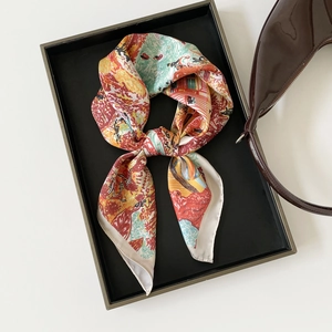 Detailed view of an artistic floral satin scarf knotted elegantly beside a brown handbag
