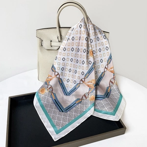 Detail of elegant satin scarf with clover print draped over a luxury leather handbag