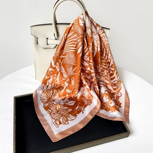 Close-up of elegant orange forest print silk scarf draped on a luxury white handbag