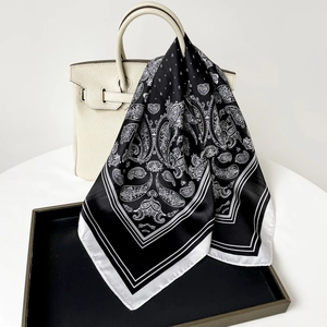 Dettaglio di un foulard in raso paisley bianco e nero drappeggiato su una borsa di lusso