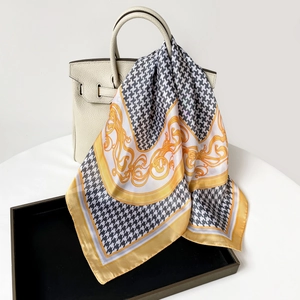 Detail of houndstooth silk scarf with baroque patterns tied on a white luxury handbag