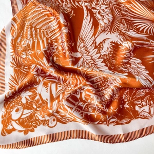 Close-up of tropical forest print on orange and white silk scarf with bird details