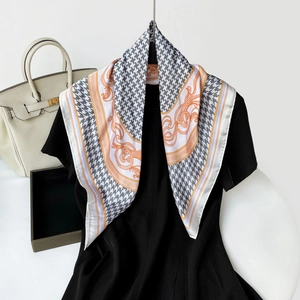Detail of houndstooth silk scarf with orange baroque border worn on a black dress neck