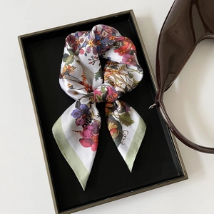 Detailed view of floral silk scarf folded in black tray next to a leather handbag