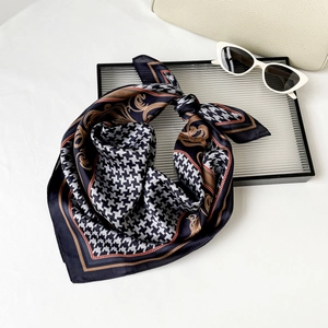Detail of silk-like square scarf with houndstooth and baroque patterns on a glass tray