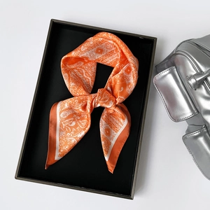 Detailed view of orange paisley satin scarf displayed on a tray with silver handbag