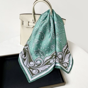 Detail of mint green paisley silk scarf elegantly draped over a white leather luxury handbag