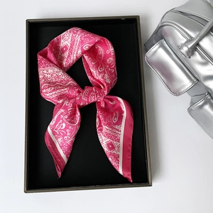 Detail of fuchsia paisley satin scarf tied in a knot beside a silver handbag
