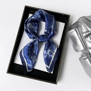 Close-up of navy blue paisley satin scarf tied in a bow inside a premium black gift box