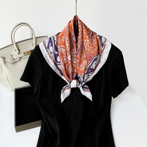 Detailed view of the vibrant orange and purple paisley silk scarf styled on a black top