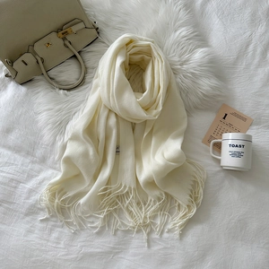 Detailed texture of cream-colored cashmere scarf with elegant tassel fringe on white fur
