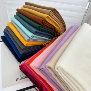 Close-up of stacked solid color cashmere scarves with fine fringe trim and soft texture