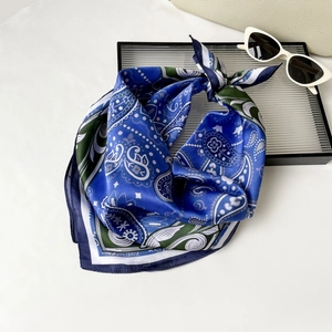 Detailed view of paisley silk scarf with blue and green patterns and white trim edge