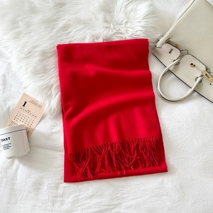 Detail of red cashmere-feel scarf featuring soft fringe tassels on white plush bedding