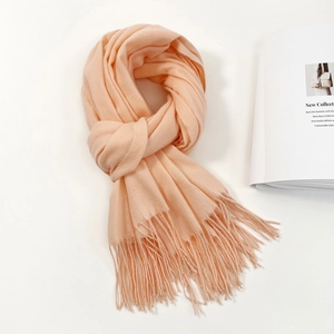 Detail of soft fringe tassels on a light apricot cashmere-feel scarf with magazine backdrop