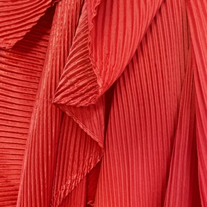 Macro shot of red pleated satin fabric with elegant vertical folds and silky sheen