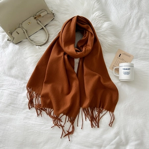 Detailed texture of caramel cashmere-like scarf with long fringe on white fur rug