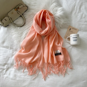 Close-up of a soft coral cashmere scarf showing fringe and premium fabric texture