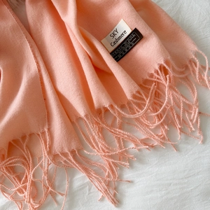Close-up of peach pink virgin wool scarf texture with soft fringe and fabric label