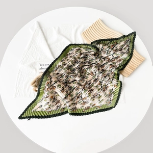 Detail of pleated silk scarf with floral print and deep green edges on white wood