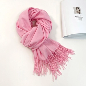 Detail view of pink cashmere-like scarf with fringe tassels next to a fashion magazine