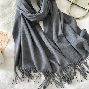 Detailed view of soft grey cashmere-like scarf with long fringe on cozy fabric background