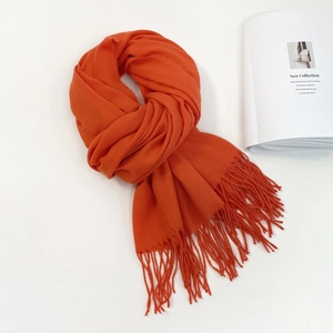 Detailed close-up of bright orange knitted scarf with fine tassels on white background