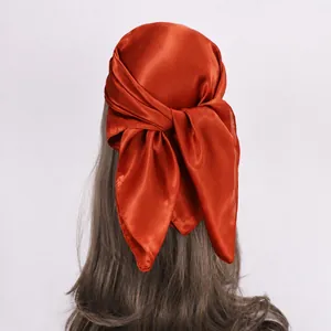 Detail of rust red satin headscarf tied on wavy brown hair with silky texture