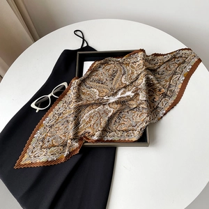 Detail of pleated silk scarf featuring golden paisley pattern on black dress background