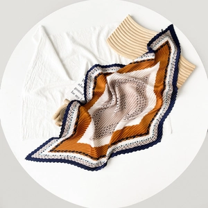 Detail of pleated silk scarf with orange and navy color blocks on a white table