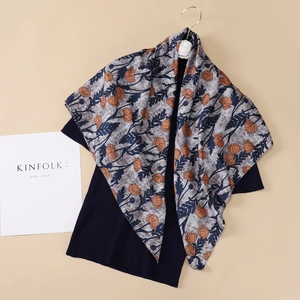 Artistic silk scarf with orange floral pattern paired with dark knitwear and magazine