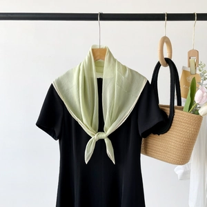 Detail of light green breathable silk scarf knotted on a black dress with woven bag