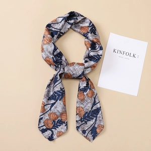 Detailed close-up of a floral silk scarf with orange blooms and navy leaves on textured fabric