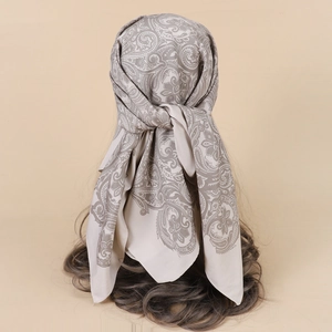 Detail of beige paisley silk-like scarf tied on a head model showing elegant styling