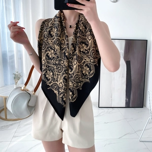 Detail of silk-like scarf worn as a shawl featuring black and gold paisley patterns