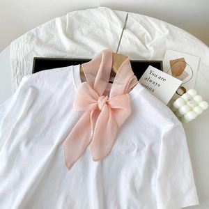 Dettaglio di un foulard in seta rosa plissettato a fiocco su una maglietta bianca