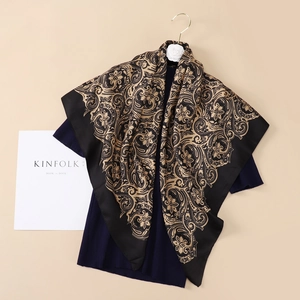 Detailed view of the black and gold paisley satin scarf draped over navy blue knitwear