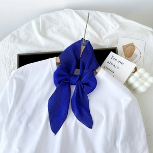 Dettaglio di un foulard in seta a pieghe blu reale annodato a fiocco su una maglia bianca