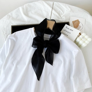 Dettaglio di un fiocco in chiffon plissettato nero abbinato a una maglia bianca