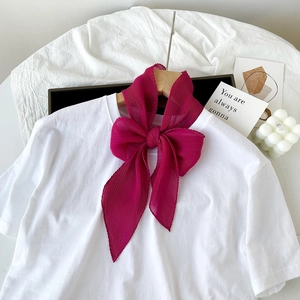 Dettaglio del foulard in seta plissettata rosso rosa annodato a fiocco su una t-shirt