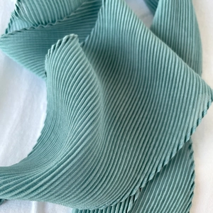Dettaglio del tessuto plissettato verde teal con trama fine e finitura delicata dell'orlo