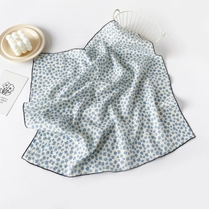 Detailed close-up of white cotton square scarf with blue floral print and black stitched edges