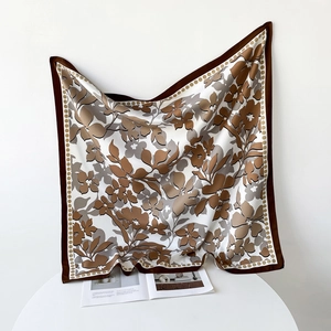 Détail d'un grand carré de soie aux motifs floraux marron drapé sur une petite table blanche