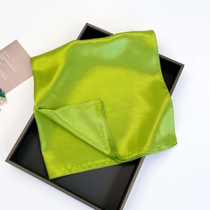 Detail of bright green satin scarf with smooth texture folded in a black gift box