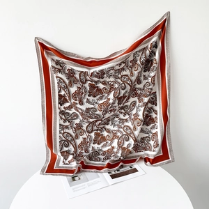 Detailed close-up of a white and rust red paisley silk scarf draped over a white table