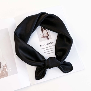 Detailed close-up of glossy black silk scarf tied in a bow with smooth satin texture