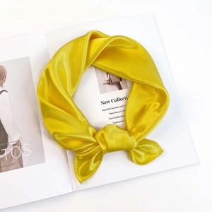 Detail of a smooth bright yellow satin neck scarf elegantly knotted on a stylish magazine