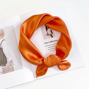 Detailed view of a bright orange satin scarf tied in a knot on a fashion magazine