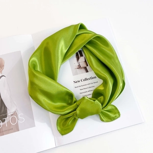 Detailed view of a bright grass green satin silk scarf knotted on a minimalist fashion magazine