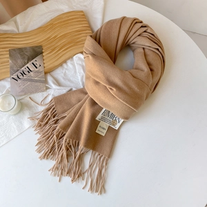 Détail d'une écharpe en cachemire camel avec franges, étiquette de marque et revue VOGUE